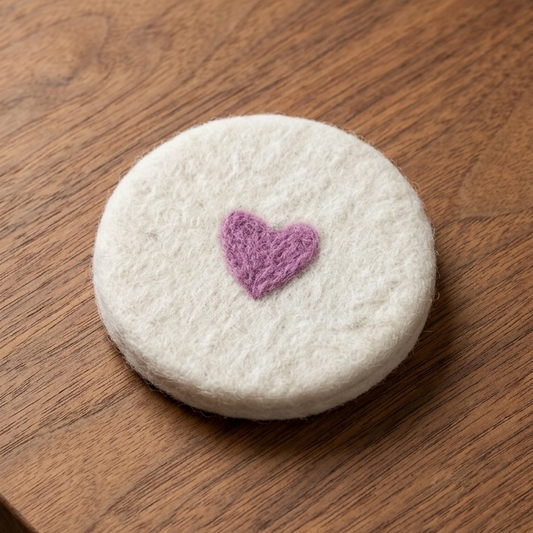 A round white felt coaster with a small purple heart in the center, resting on a brown wooden table.