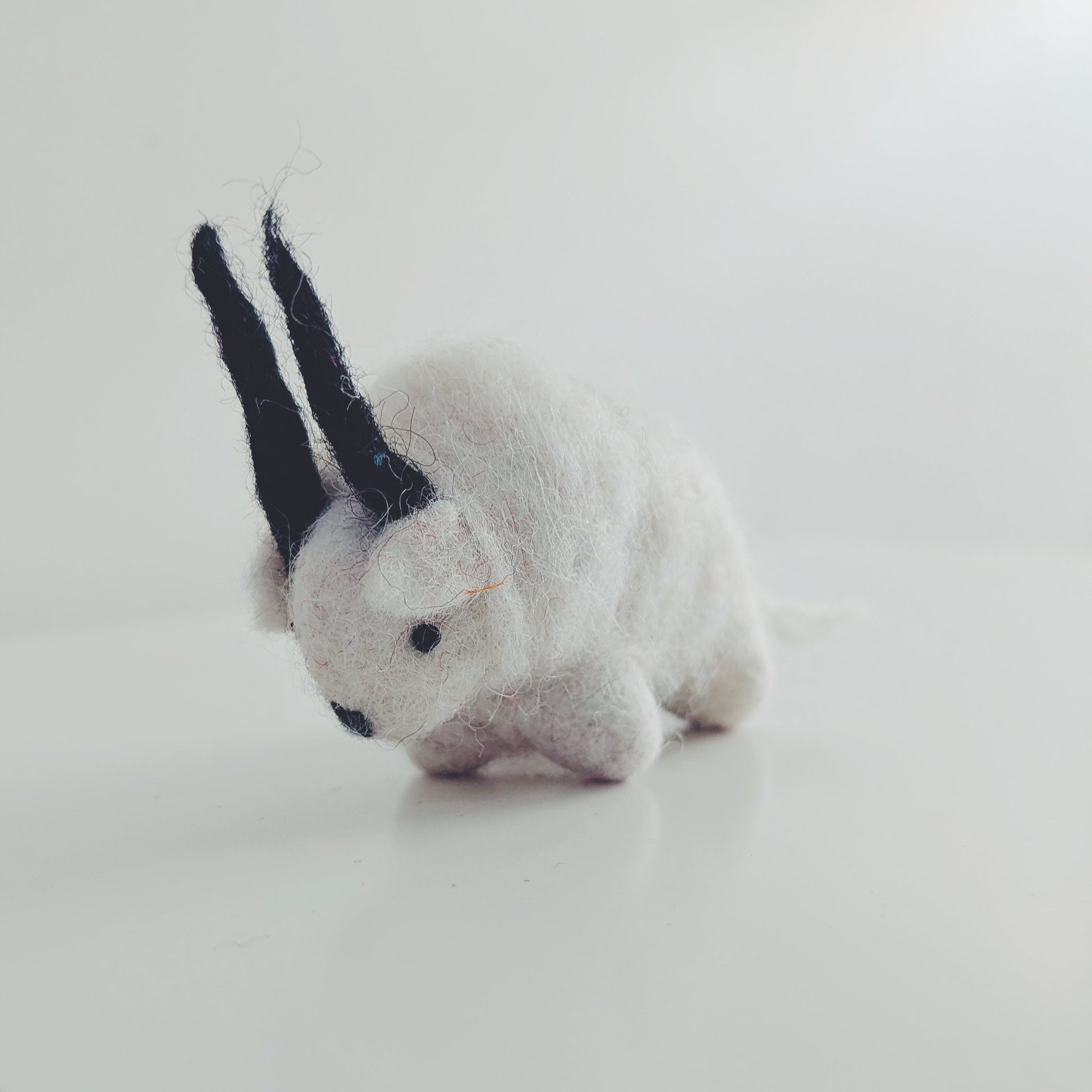 A small white felt Himalayan goat toy, photographed on a plain white surface against a white background.