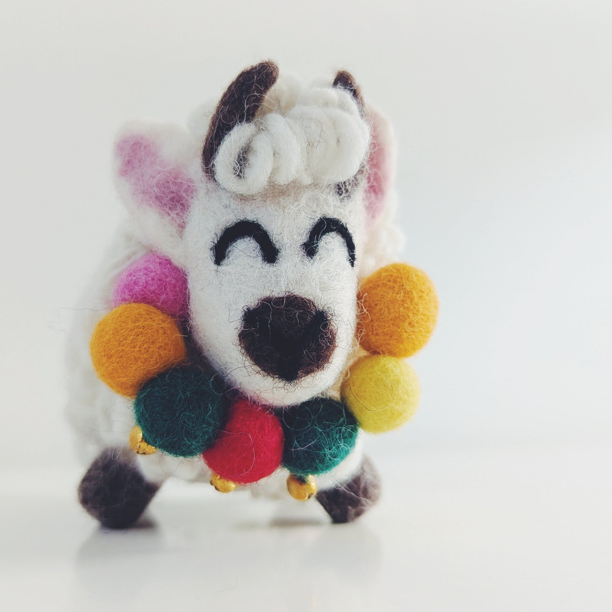 A small white felt Yak figurine with colorful pom-pom accents around its neck and ears, photographed against a plain white background.
