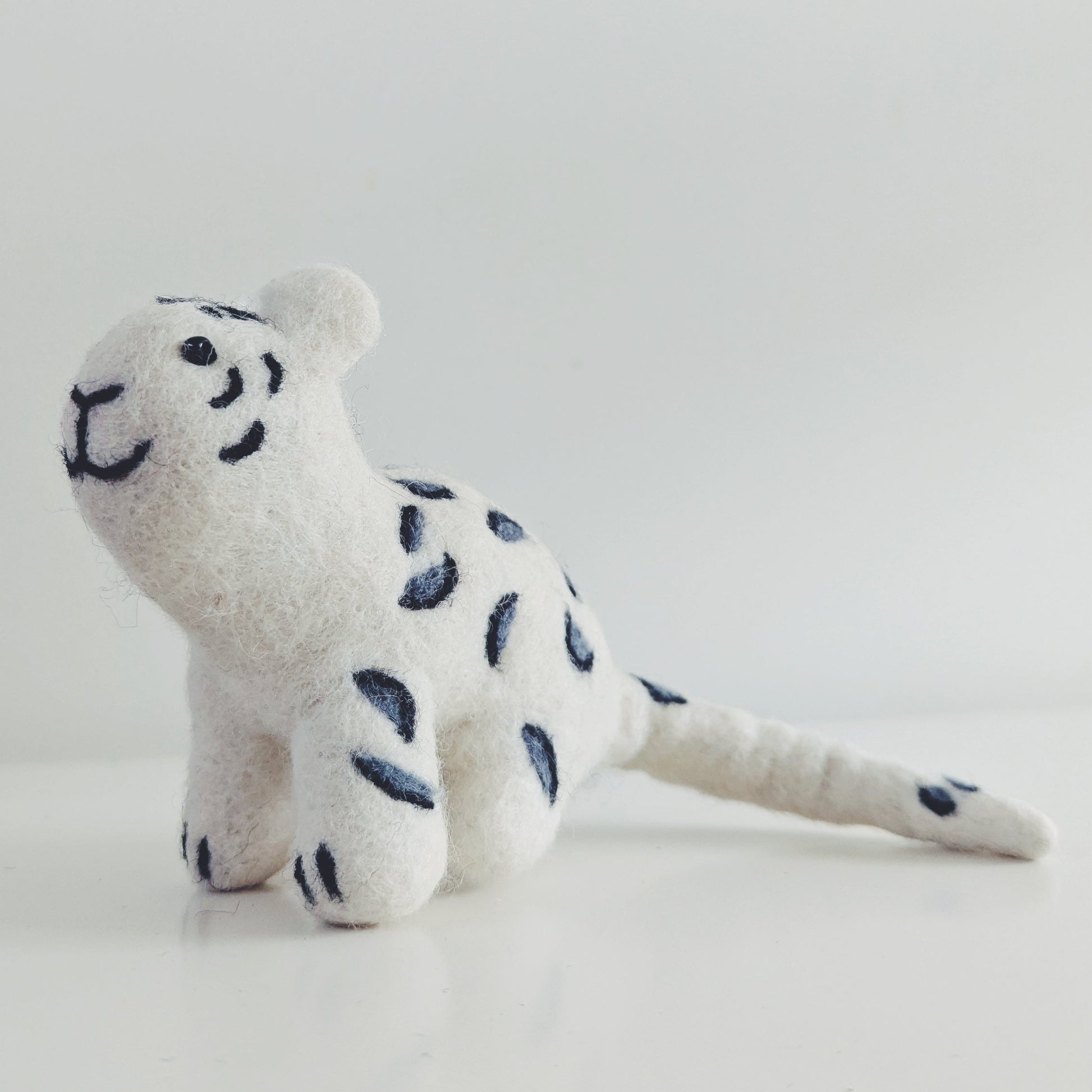 A small snow leopard felt toy with dark blue spots, photographed on a plain light background.