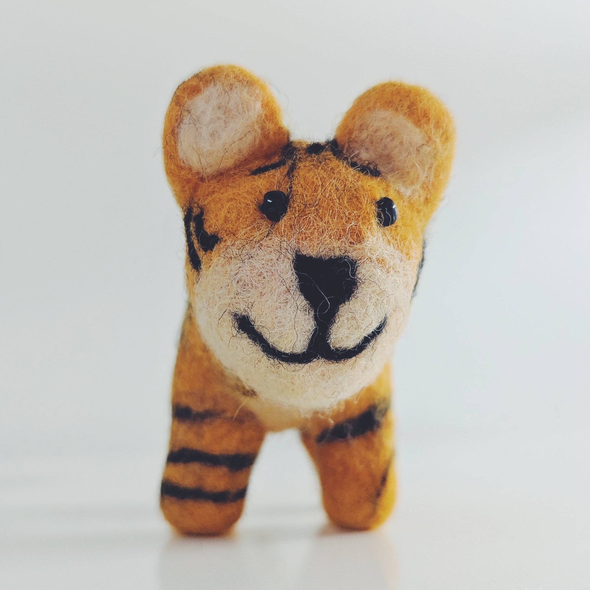 A small felt tiger figurine with orange and black stripes, standing against a plain white background.
